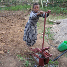 A picture of a young girl with her hands on the handle bar of a treadle pump and her feet on the pedals.