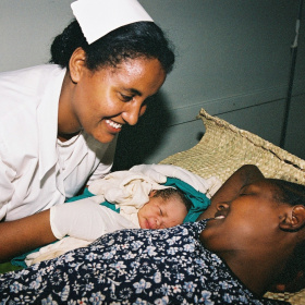 A nurse is smiling and leaning over a woman and her new born baby.