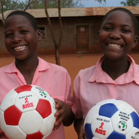 A close up of two children standing next to each other holding footballs and smiling with joy.