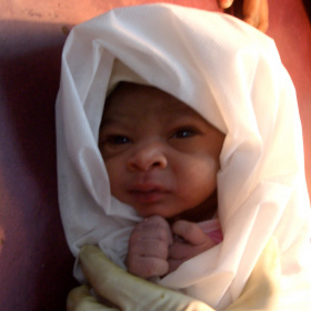 A newborn baby with a white blanket wrapped around them.