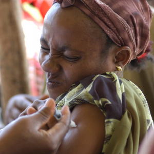 A close up picture of a woman receiving an injection in her arm and squeezing her eyes tight shut in pain.