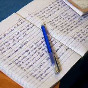 A close up picture of an open notebook, the pages filled with handwriting and a blue pen lying across the middle.