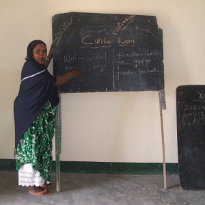 A woman is standing next to a chalk boards with words written on it. She is looking at the camera and smiling.