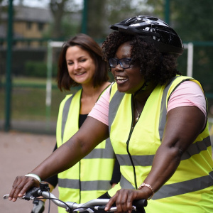 A picture of a young woman on a bike smiling. Behind her you can see an instructor watching and smiling.