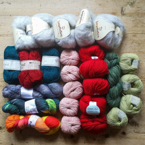 A picture of lots of balls and hanks of yarn laid out on a table. 