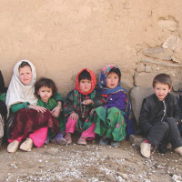 A picture of five young children sat against a crumbling wall with rubble on the ground in front of them.