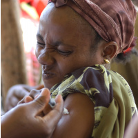 A close up picture of a woman receiving an injection in her arm and squeezing her eyes tight shut in pain.