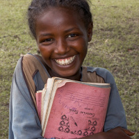 A close up shot of a young girl holding some notebooks to her chest, with a big smile on her face.