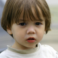 A close up picture of a young boy with long hair and big eyes, looking sad.
