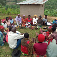 A picture of a group of people sat in a circle, engaged in discussion. Crops are visible behind them in the background.
