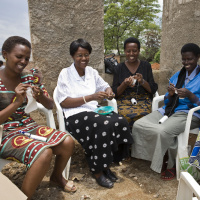 Four women are sat in a semi circle knitting outdoors, they are all smiling and look very happy.
