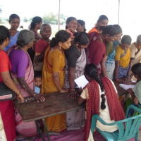 A queue of women of all ages standing in front of a table where there are two people filling out forms.