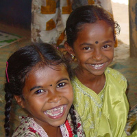 A picture of two young Indian girls looking into the camera and smiling widely.