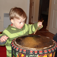 A young child is holding a drumstick and using it to bang a large drum.