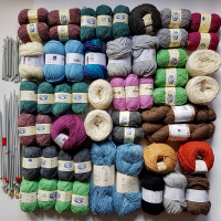 A picture of lots of different coloured balls of yarn laid out on a white background. To the left are several pairs of crochet hooks and knitting needles.