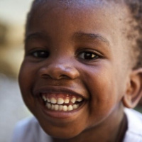 A close up of a young child who is smiling and showing all his teeth.